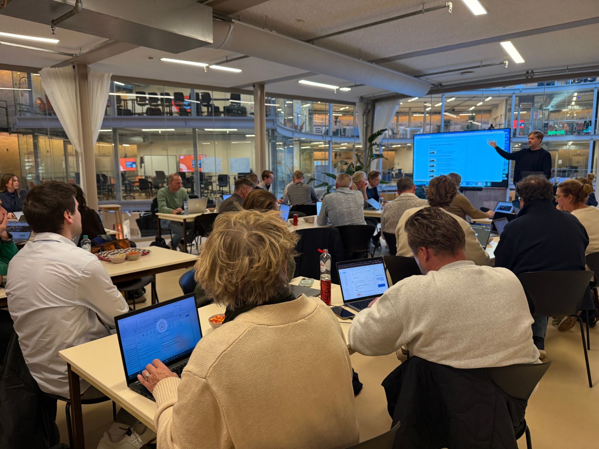 Volle zaal in De Koepel in Haarlem: deelnemers aan laptops, de trainer wijst iets aan op het scherm